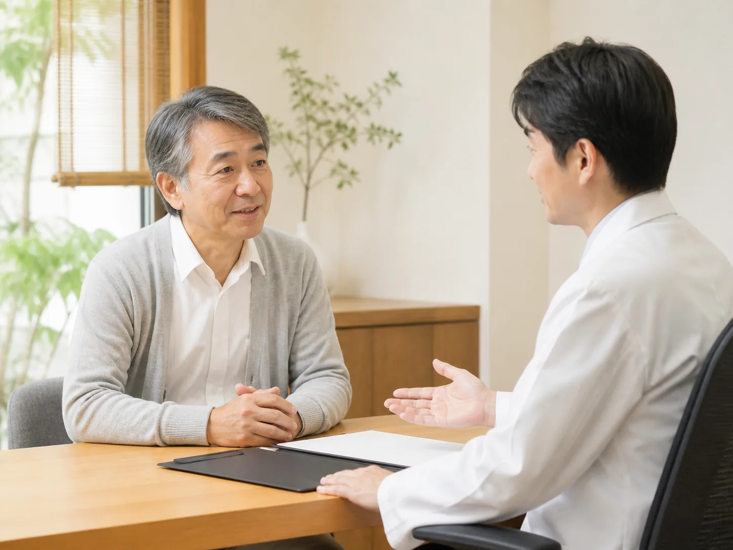 診察室で白衣のスタッフと向かい合って話す高齢の男性のイメージ