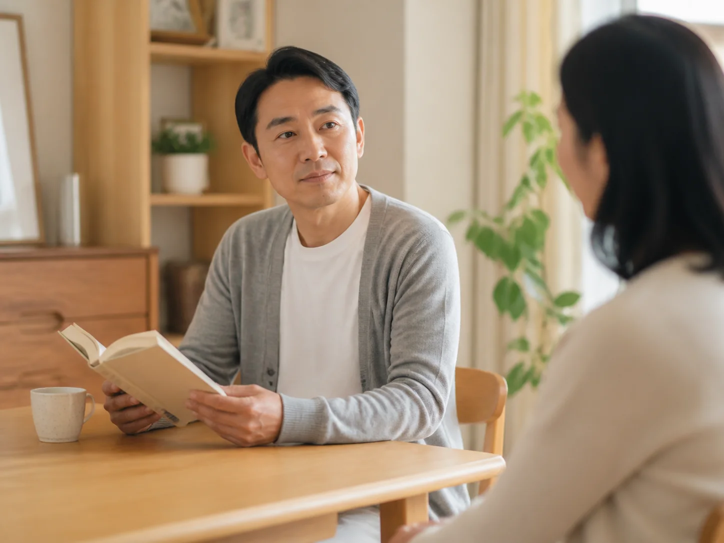 自宅のテーブルで本を読む男性と、向かいに座る女性のイメージ