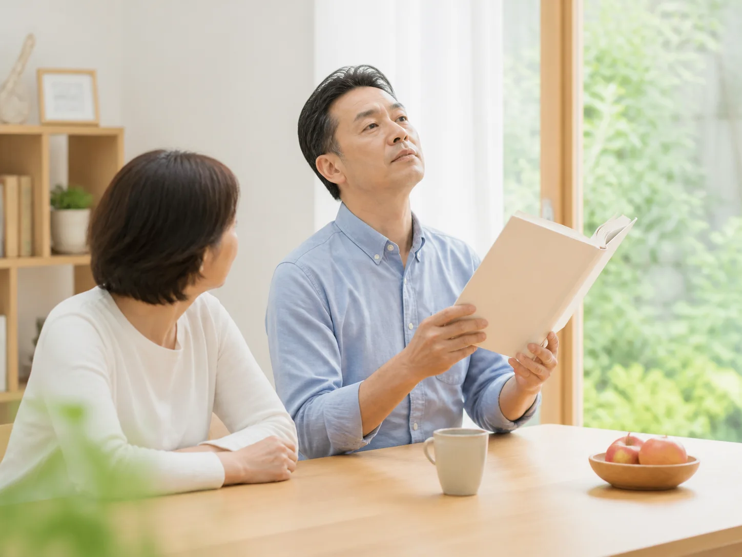 自宅で本を持ち、顔を上向きにして読む男性と、そばに座る女性のイメージ